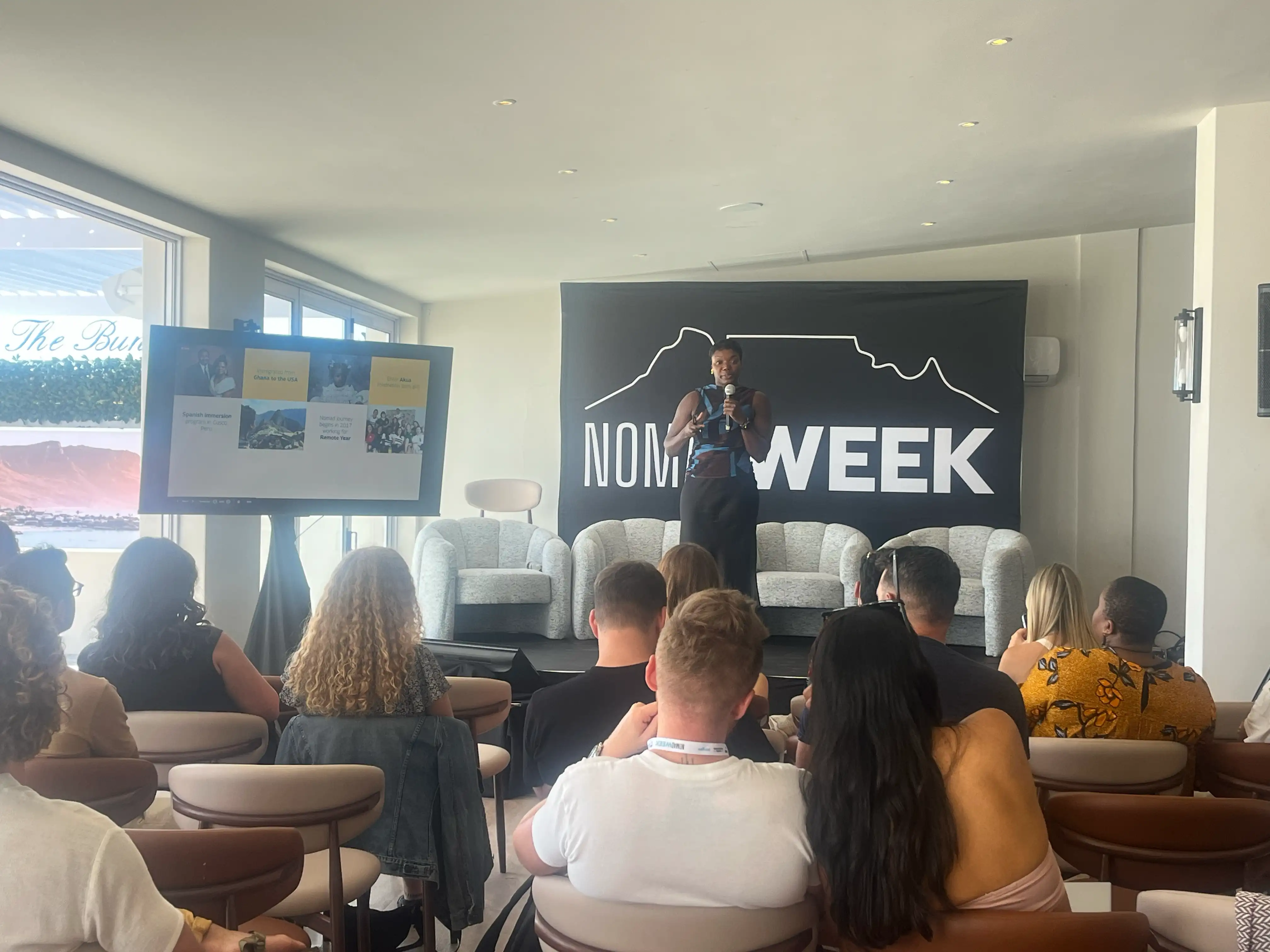 Speaker on stage at Nomad Week in Cape Town with Table Mountain logo on backdrop and presentation screen