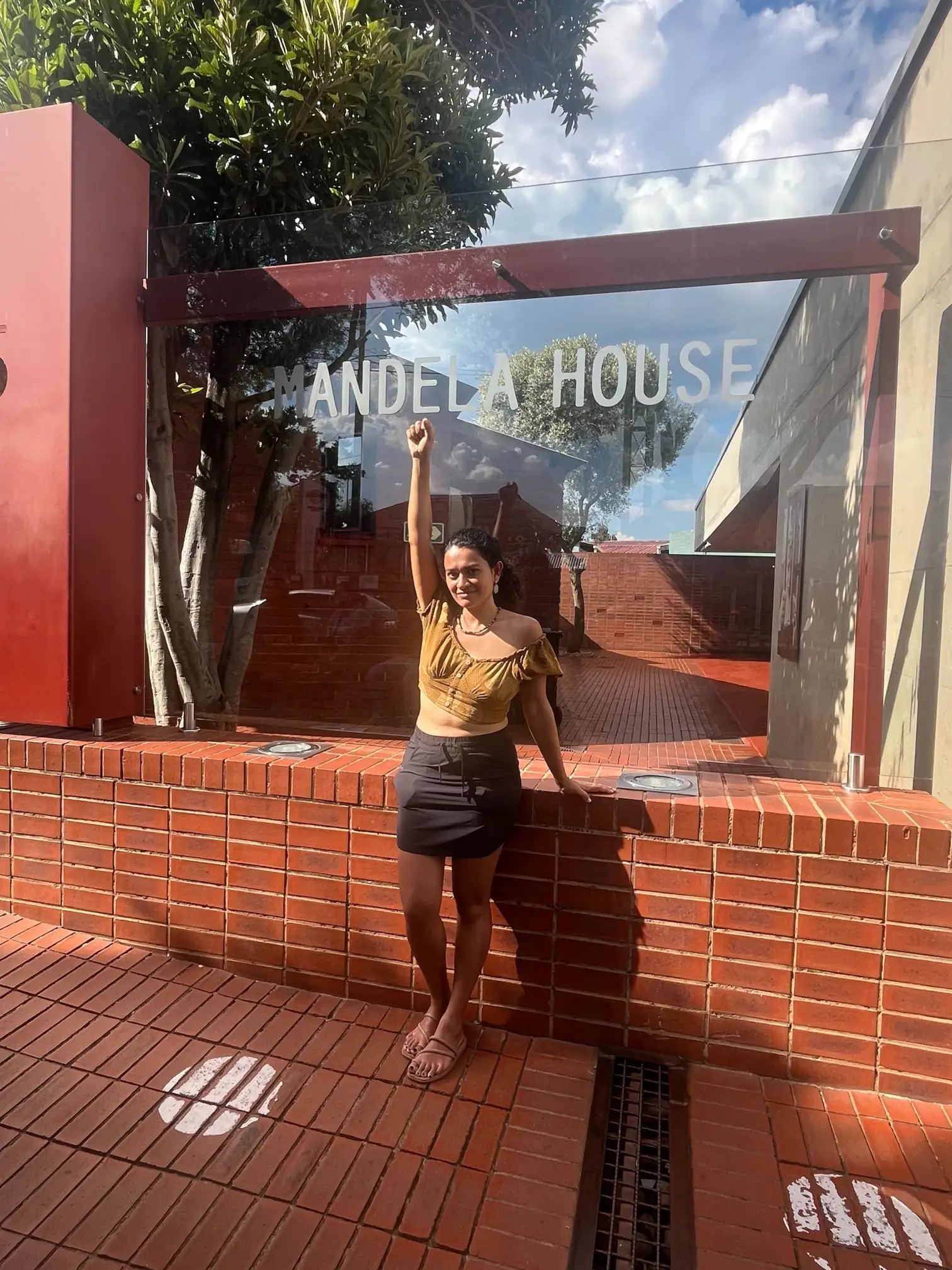Visitor raising a fist in front of the Mandela House glass sign in Soweto