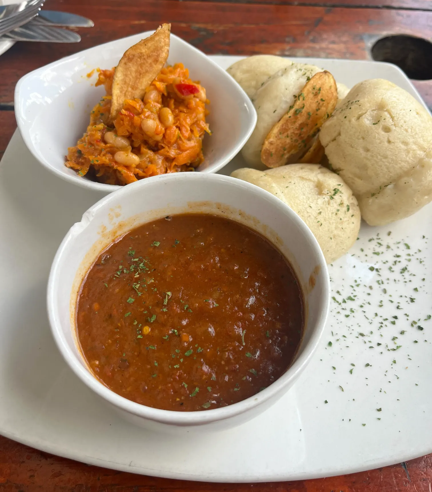 Traditional South African meal with chakalaka relish, steamed bread rolls, and tomato stew on a white plate