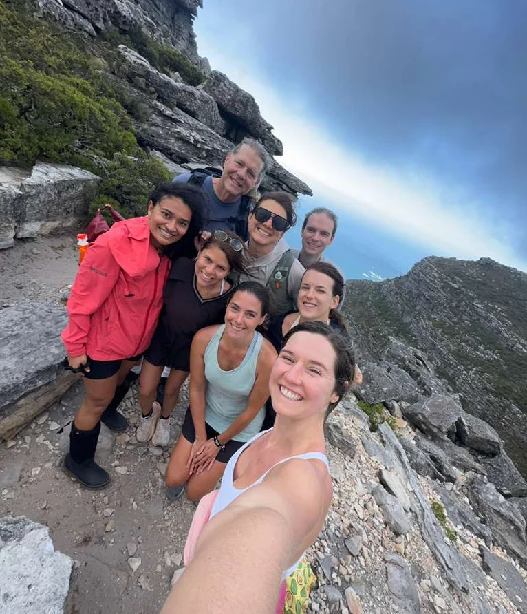 Group of hikers smiling for a selfie on a rocky mountain trail above the ocean near Cape Town