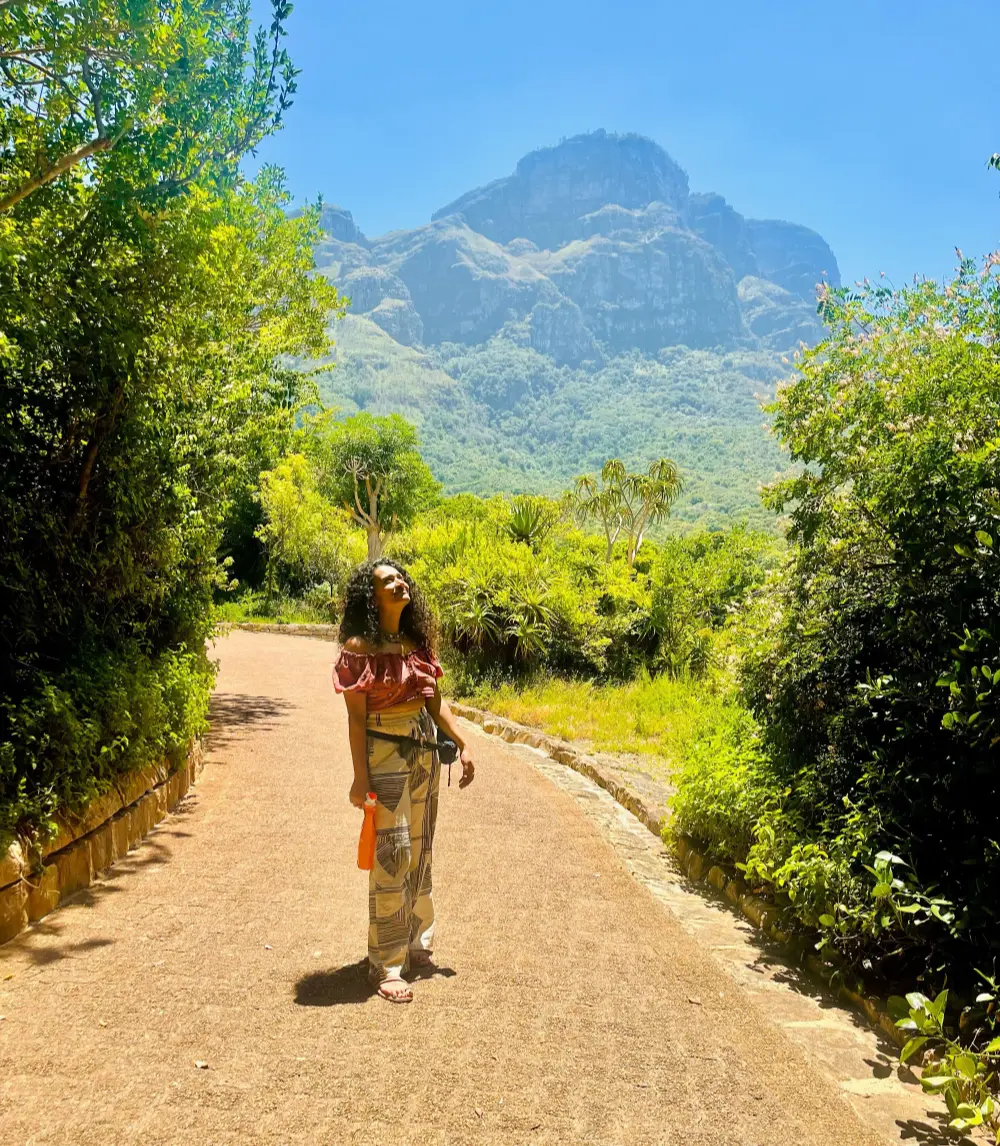 Woman on a sunlit path at Kirstenbosch Botanical Garden with Table Mountain rising behind trees
