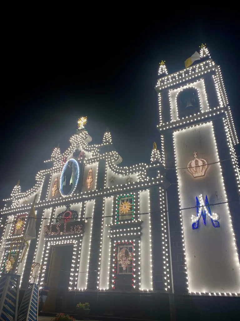 Igreja de Nossa Senhora da Luz in the Azores at night outlined in glowing white festive lights, with N. S. LUZ spelled in lights above the entrance