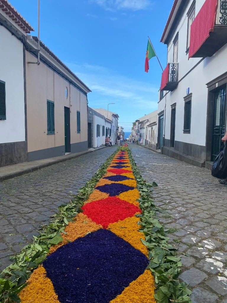 Geometric floral carpet in purple orange and green along an Azorean cobblestone street leading toward the Atlantic