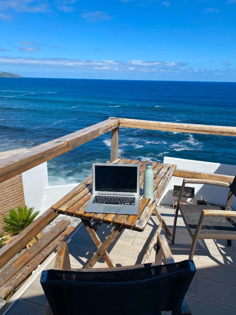 Laptop and water bottle on a wooden balcony table overlooking the Atlantic from São Miguel, Azores