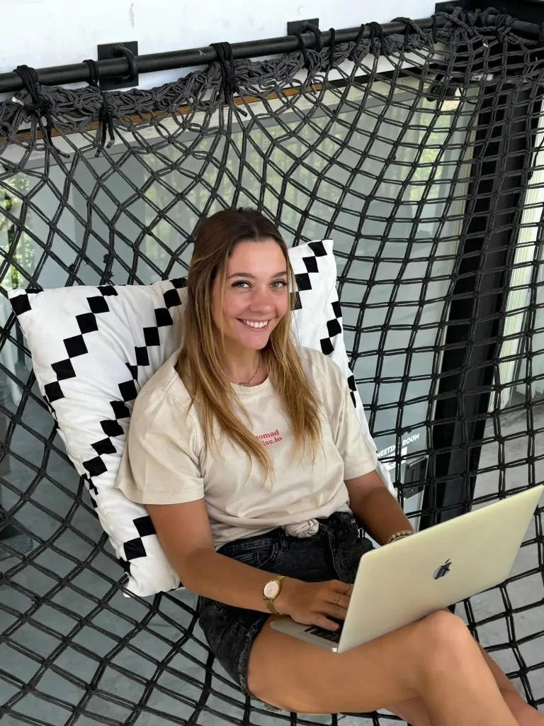 Leonie working on a laptop in a hammock-style net chair, nomadwise.io on her shirt