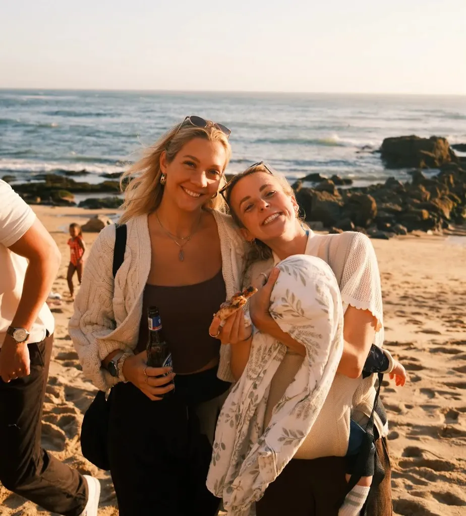 Two friends on a sandy beach at golden hour by the ocean in Portugal
