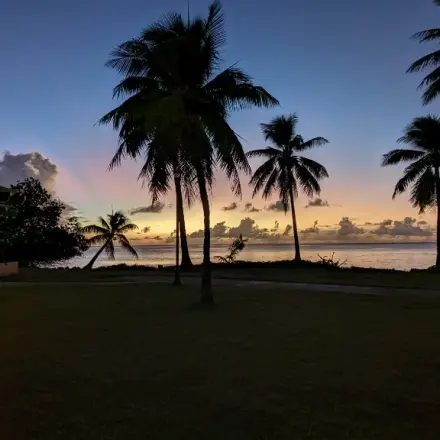 Sunset over Micro Beach, Saipan, with palm trees against an orange and purple sky