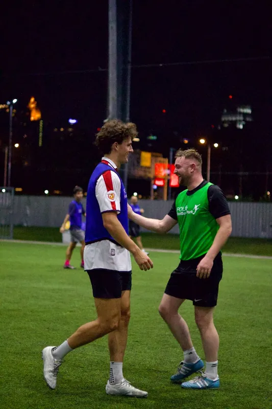 Two smiling players greet each other during a night pickup football game at Polo Football Park in Bangkok