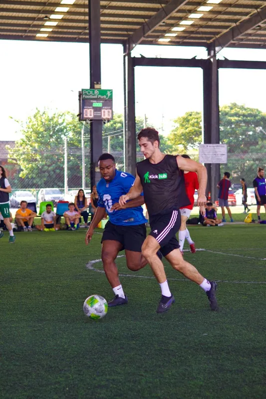Two players compete for a football during a KickHub pickup game at Polo Football Park in Bangkok, one wearing a black KickHub bib