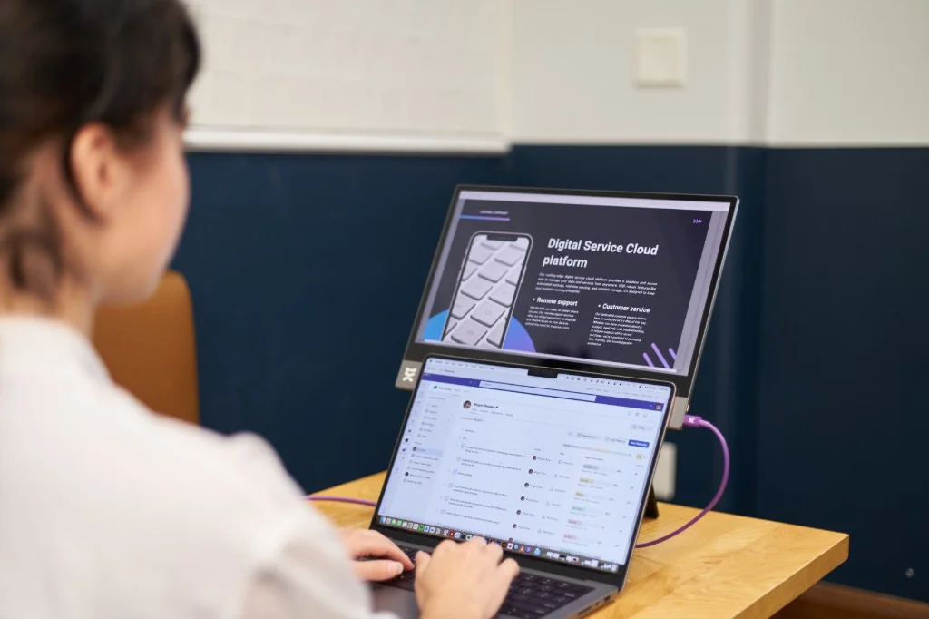 Remote worker using a laptop with a portable monitor stacked above it in a coworking space